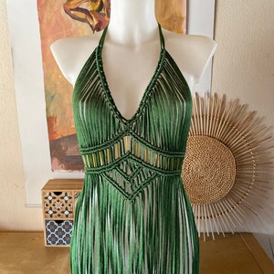 Op de afbeelding: Een groene gehaakte haltertop met gouden kralen en franjes. De top is op een wit mannequin.