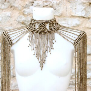 Op de afbeelding: Een beige macram&eacute; choker ketting met lange franjes. De ketting wordt gedragen door een wit mannequin.
