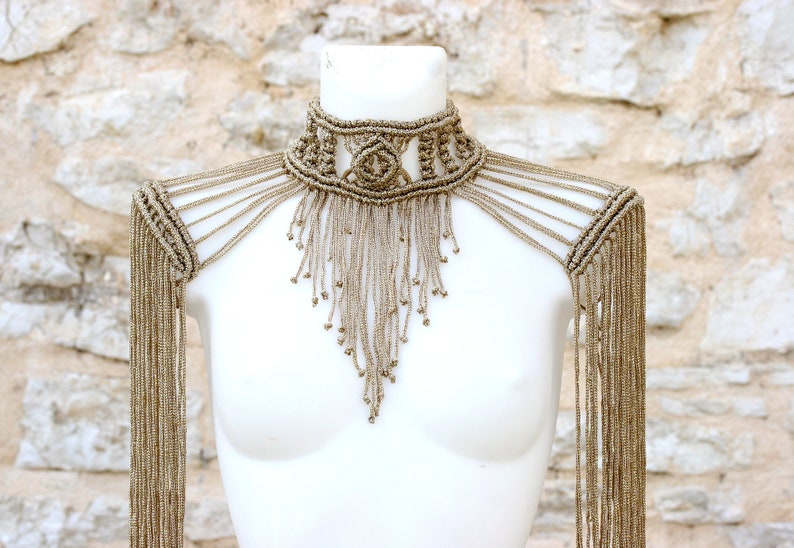 Op de afbeelding: Een beige macram&eacute; choker ketting met lange franjes. De ketting wordt gedragen door een wit mannequin.