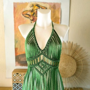 Op de afbeelding: Een groene gehaakte haltertop met franjes. De top is gemaakt met een macram&eacute;-techniek en heeft een geometrisch patroon.