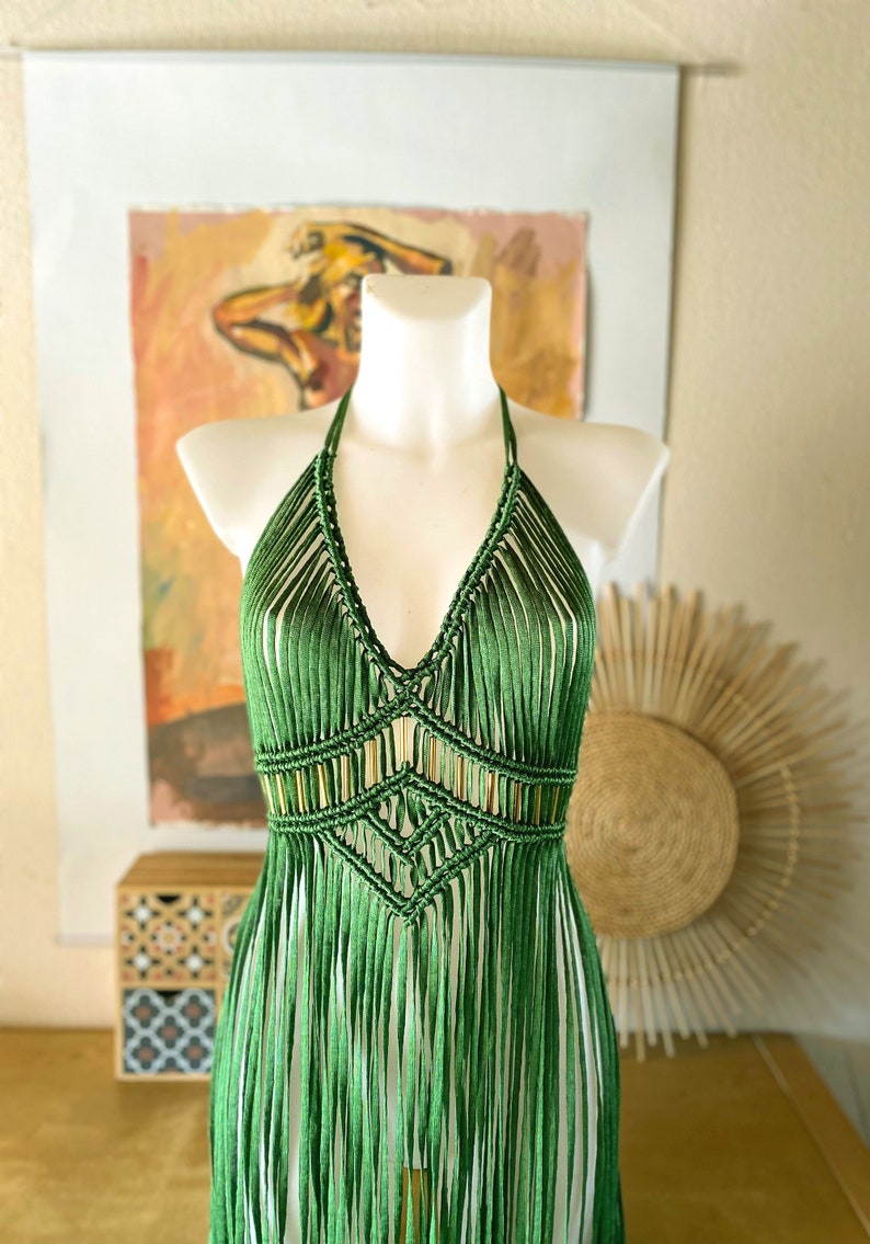 Op de afbeelding: Een groene gehaakte haltertop met franjes. De top is gemaakt met een macram&eacute;-techniek en heeft een geometrisch patroon.
