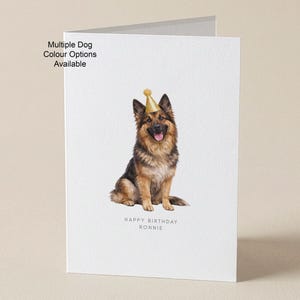 May include: A white birthday card featuring a German Shepherd wearing a gold party hat. The card reads "Happy Birthday Ronnie." Text on the card reads "Multiple Dog Colour Options Available."
