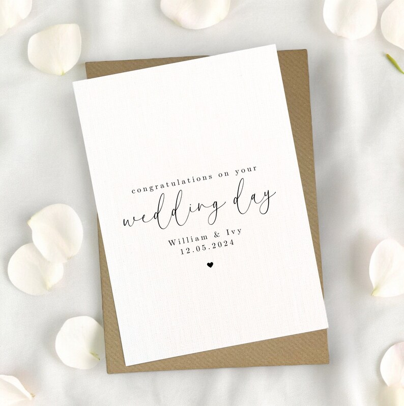 May include: A white card with black text that reads "congratulations on your wedding day" with the names "William & Ivy" and the date "12.05.2024" below. The card is sitting on a brown envelope.