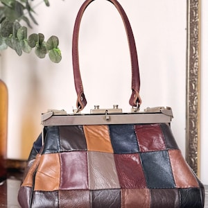 Peut inclure: Un sac à main vintage en cuir patchwork avec une fermeture à fermoir en métal et une poignée en cuir bordeaux. Le sac présente une variété de carrés de cuir dans les tons marron, beige, bordeaux et noir.