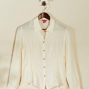 May include: A white long-sleeved button-down shirt with a gathered waist and gold buttons.