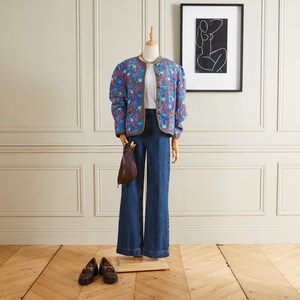 Puede incluir: Una chaqueta acolchada azul con estampado floral, una camiseta blanca, unos vaqueros azules y mocasines marrones. La chaqueta tiene un ribete verde y un cierre de botón.