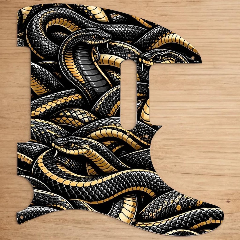 May include: A guitar pickguard featuring a detailed illustration of intertwined snakes. The design showcases black snakes with gold and yellow accents, creating a striking contrast. The pickguard is set against a wooden background.