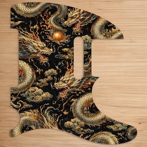 Könnte beinhalten: Ein Gitarren-Schlagbrett mit schwarzem Hintergrund und einem detaillierten goldenen Drachendesign. Die Drachen sind mit Wolken und einer goldenen Kugel verwoben. Das Schlagbrett hat eine einzigartige Form mit einer gebogenen Oberseite und einem spitzen Boden.