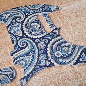 Op de afbeelding: Een gitaar slagplaat met paisley patroon in marineblauw, lichtblauw en wit. De slagplaat heeft een unieke vorm met een gebogen bodem en een gedeelte voor de pickups. Een kleiner bijpassend stuk is ook aanwezig.
