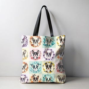 K&ouml;nnte beinhalten: Eine Tragetasche mit einem sich wiederholenden Muster von Boston Terrier-Portr&auml;ts in Blumenkr&auml;nzen. Die Tasche hat schwarze Griffe und einen cremefarbenen Hintergrund mit Pastellquadraten.