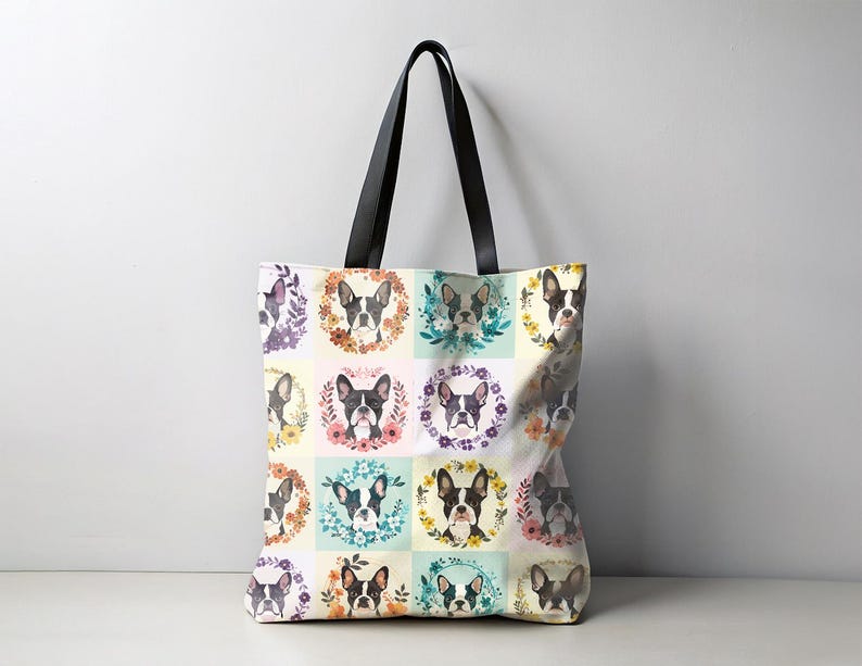 K&ouml;nnte beinhalten: Eine Tragetasche mit einem sich wiederholenden Muster von Boston Terrier-Portr&auml;ts in Blumenkr&auml;nzen. Die Tasche hat schwarze Griffe und einen cremefarbenen Hintergrund mit Pastellquadraten.