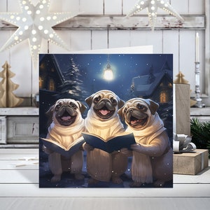 May include: A Christmas card featuring three pugs dressed in white robes and scarves, singing carols from a book under a streetlight in a snowy village.