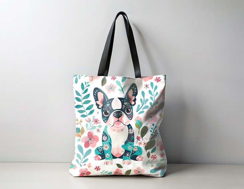 Puede incluir: Una bolsa de tela blanca con asas negras presenta una ilustraci&oacute;n colorida de un bulldog franc&eacute;s con detalles florales. El perro lleva una camisa con estampado azul y verde.