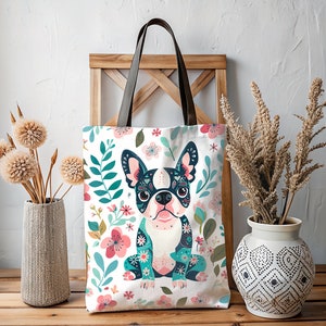 Puede incluir: Una bolsa de lona blanca con un patr&oacute;n floral y una imagen de dibujos animados de un bulldog franc&eacute;s. El bulldog lleva un patr&oacute;n floral azul y verde y tiene ojos negros y una nariz rosa.