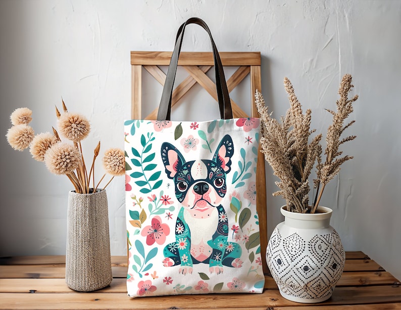 Puede incluir: Una bolsa de lona blanca con un patr&oacute;n floral y una imagen de dibujos animados de un bulldog franc&eacute;s. El bulldog lleva un patr&oacute;n floral azul y verde y tiene ojos negros y una nariz rosa.