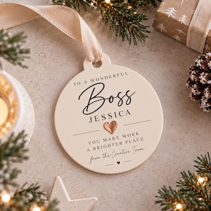 Può includere: Un ornamento rotondo in ceramica color crema con testo nero che recita TO A WONDERFUL Boss JESSICA YOU MAKE WORK A BRIGHTER PLACE from the Creative Team, decorato con un piccolo cuore in metallo color oro rosa e un nastro beige per appenderlo.