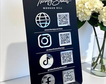 Op de afbeelding: Een verticaal zwart rechthoekig bord met afgeronde hoeken, voorzien van zilverkleurige 3D-socialemedia-iconen en QR-codes. Tekst bevat TS Therapy Services, Morgan Hill, website, social media handles en Robert Freitas, LCSW - Licensed Therapist.