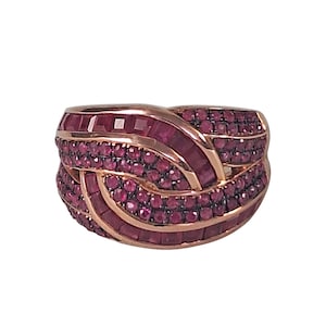 Op de afbeelding: Een roségouden ring met een gevlochten ontwerp, bezet met talrijke kleine, ronde en rechthoekige robijnen. De robijnen hebben een dieprode kleur, wat een sterk contrast vormt met het goud.