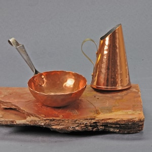 May include: A hammered copper ladle with a silver handle and a hammered copper pitcher with a brass handle on a brown stone surface.