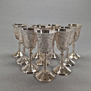 Puede incluir: Conjunto de diez copas de plata con intrincados diseños florales. Las copas están dispuestas en círculo sobre un fondo gris.