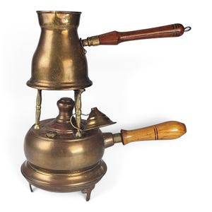 May include: A brass coffee maker featuring a rounded base with a light wood handle and a top pot with a dark wood handle. The two sections are connected by three thin brass pillars, and a small brass funnel is attached to the side of the base.