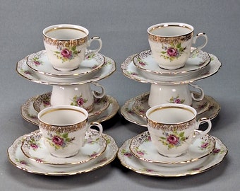 Könnte beinhalten: Sechs weiße Teetassen und Untertassen mit goldenen Verzierungen und Blumendesigns. Die Tassen und Untertassen sind paarweise auf einer grauen Oberfläche angeordnet.