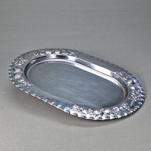 May include: A silver oval serving tray with a decorative embossed floral design around the edge.