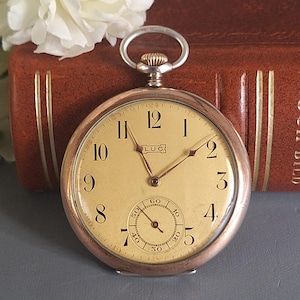 May include: A silver pocket watch with a white face and black Roman numeral hour markers. The watch has a small second hand dial at the bottom and the word "LUC" printed on the face.