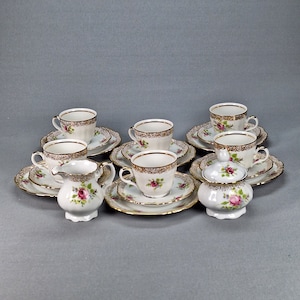 May include: A set of white porcelain teacups and saucers with gold trim and floral designs. The set includes a creamer and sugar bowl.
