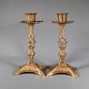 Puede incluir: Dos candeleros dorados. Cada uno tiene una base ornamentada, un tallo decorativo con diseño de diamante y una parte superior en forma de copa para una vela. Los candeleros de metal tienen un aspecto vintage y son ideales para la decoración del hogar.