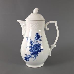 May include: A white porcelain coffee pot with a blue floral design. The pot has a lid with a small bird finial and a delicate handle.