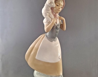 May include: A porcelain figurine of a girl wearing a pink and white dress and a pink bonnet, carrying a white lamb on her shoulders.