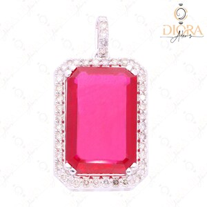 May include: A rectangular pendant with a vibrant pink gemstone center, framed by a halo of small, sparkling diamonds. The pendant is set in a silver-toned metal and features a matching diamond-studded bail for a necklace chain.
