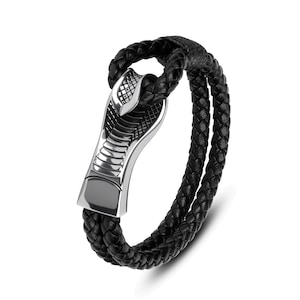May include: Black leather bracelet with a silver cobra head clasp. The bracelet features a braided design with two strands of leather. The cobra head clasp is detailed with scales and a polished finish. A stylish accessory.