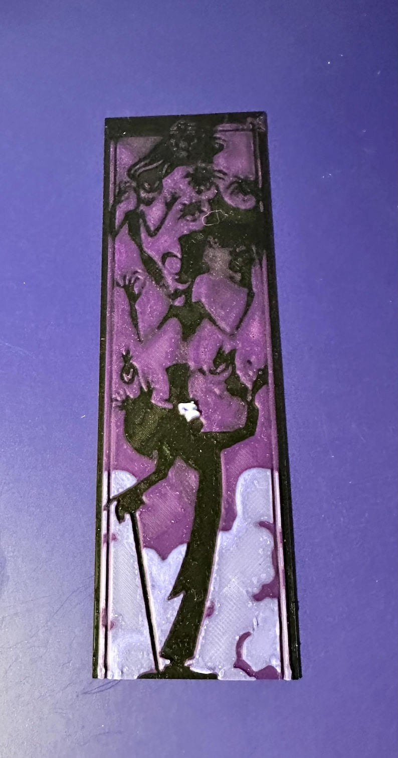 Puede incluir: Una pieza decorativa rectangular negra y morada que presenta una silueta de un hombre con bast&oacute;n y sombrero de copa, rodeado de otras figuras. El fondo es un degradado de morado y blanco.