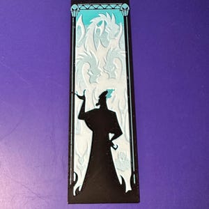 Puede incluir: Un marcap&aacute;ginas negro con la silueta de un personaje con un abrigo largo, sobre un fondo de dragones blancos y un cielo turquesa. El marcap&aacute;ginas tiene un borde negro con elementos decorativos.