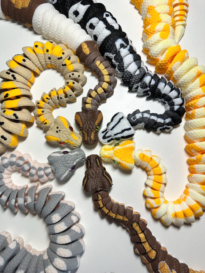 Puede incluir: Una colecci&oacute;n de juguetes de serpiente articulados y coloridos, con varios patrones y colores. Las serpientes presentan escamas detalladas y dise&ntilde;os de cabeza realistas. Los colores incluyen negro y blanco, amarillo y blanco, marr&oacute;n y amarillo, y gris.