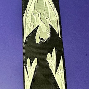 Puede incluir: Un emblema rectangular negro con un dise&ntilde;o plateado en forma de murci&eacute;lago. El emblema tiene una superficie texturizada y est&aacute; sobre un fondo p&uacute;rpura. El dise&ntilde;o del murci&eacute;lago est&aacute; detallado con un estilo arquitect&oacute;nico g&oacute;tico.