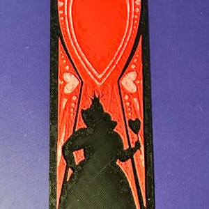 Puede incluir: Una pieza decorativa rectangular negra y roja con la silueta de la Reina de Corazones de Alicia en el pa&iacute;s de las maravillas. El dise&ntilde;o incluye un gran coraz&oacute;n rojo y peque&ntilde;os detalles de coraz&oacute;n.
