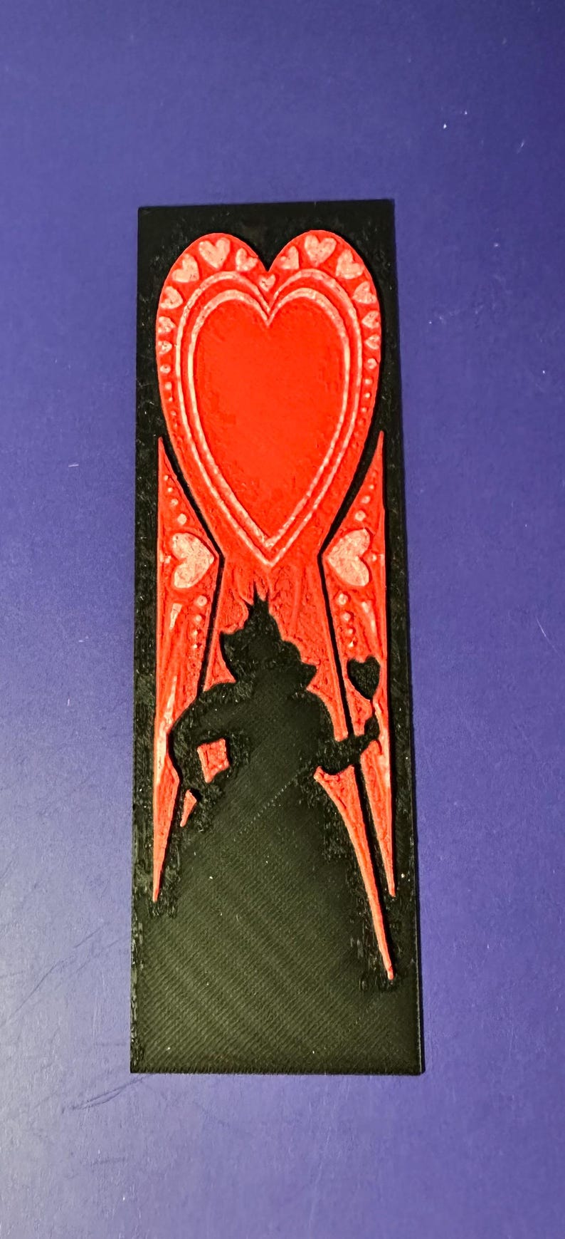 Puede incluir: Una pieza decorativa rectangular negra y roja con la silueta de la Reina de Corazones de Alicia en el pa&iacute;s de las maravillas. El dise&ntilde;o incluye un gran coraz&oacute;n rojo y peque&ntilde;os detalles de coraz&oacute;n.