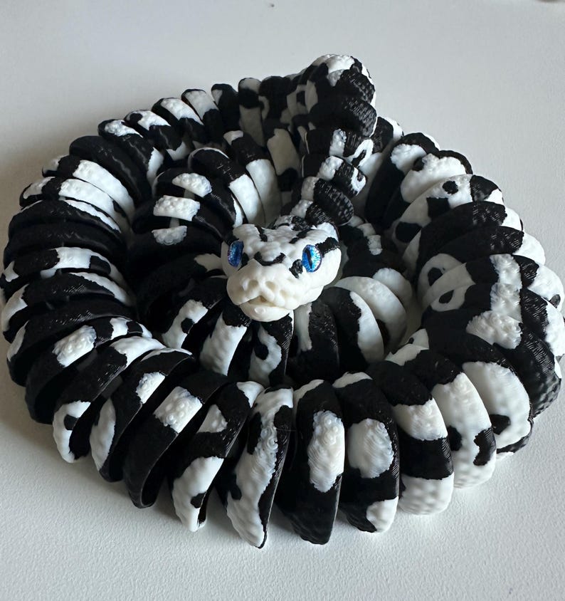 Puede incluir: Escultura de serpiente enroscada en blanco y negro, con un patr&oacute;n detallado. La cabeza de la serpiente est&aacute; en el centro, con ojos azules. La escultura est&aacute; hecha de un material que parece ser impreso en 3D.