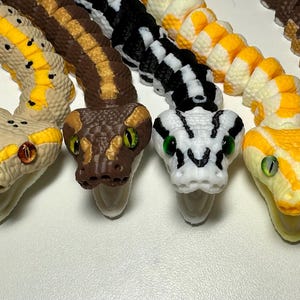 Puede incluir: Colecci&oacute;n de figuras de serpientes coloridas y detalladas. Las serpientes var&iacute;an en color, incluyendo gris, beige, marr&oacute;n, negro y amarillo, con patrones intrincados y ojos realistas. Cada serpiente est&aacute; curvada.