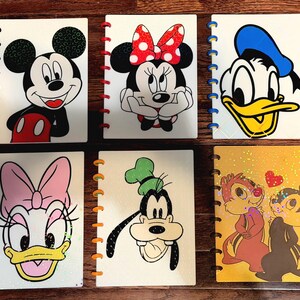 May include: Six rectangular notebooks with disc-bound spines featuring Disney characters. The covers display Mickey Mouse, Minnie Mouse, Donald Duck, Daisy Duck, Goofy, and Chip 'n Dale. Each notebook has a white or yellow background with colorful character illustrations and plastic binding discs.
