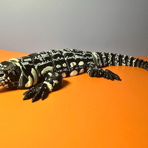 May include: An articulated lizard figurine featuring a high-contrast black and white patterned body. The reptile has a segmented design along its back and tail, allowing for flexible movement, with detailed scales and a realistic head shape.