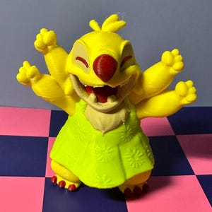 May include: A yellow figurine of a cartoon character with six arms, a red nose, and a green dress. The figurine is smiling with its mouth open. The background is a checkered pattern of pink and blue squares.