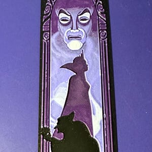 Puede incluir: Una pieza decorativa rectangular negra y morada con una imagen estilizada de un personaje de cuento de hadas. El dise&ntilde;o incluye una cara, una silueta de una figura y una silueta oscura.