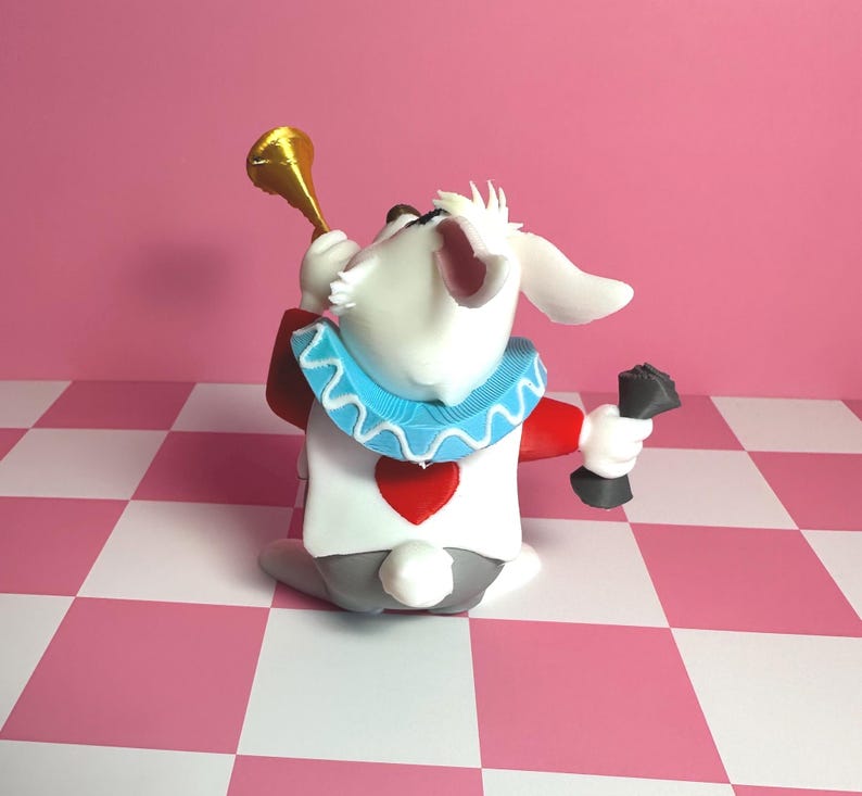 Pode incluir: Uma figura extravagante do Coelho Branco de Alice no Pa&iacute;s das Maravilhas. O coelho &eacute; branco com uma roupa vermelha e branca, uma gola azul com babados e uma trombeta dourada. Ele segura um objeto preto na m&atilde;o direita, em um fundo xadrez rosa e branco.