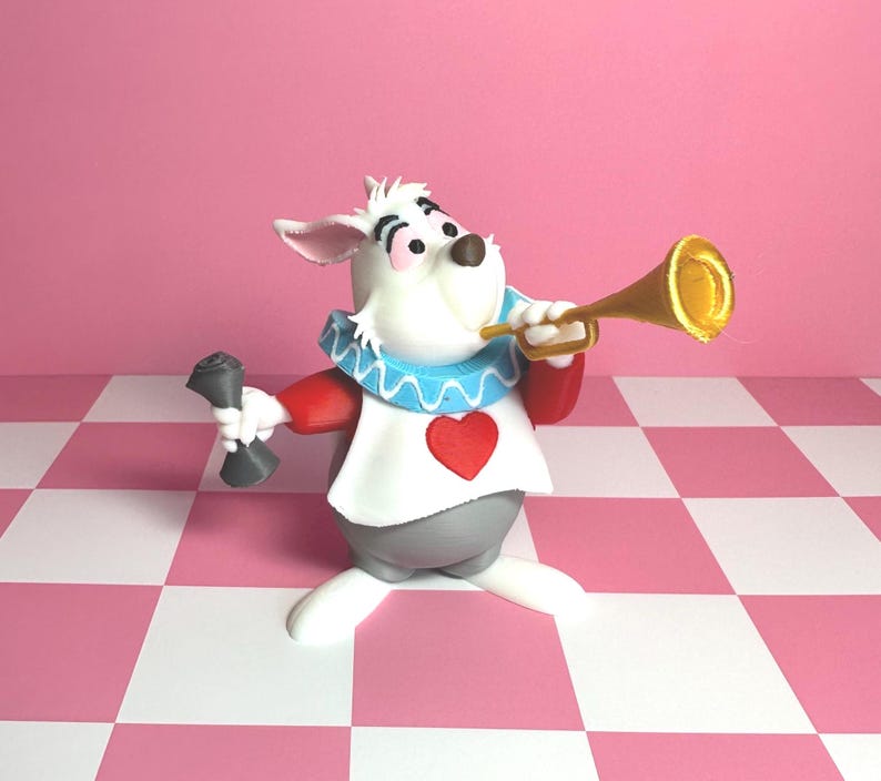 Pode incluir: Uma figura extravagante do Coelho Branco de Alice no Pa&iacute;s das Maravilhas. O coelho branco usa uma roupa vermelha e branca com uma gola azul com babados e um cora&ccedil;&atilde;o vermelho. Ele segura uma trombeta dourada e um objeto cinza.