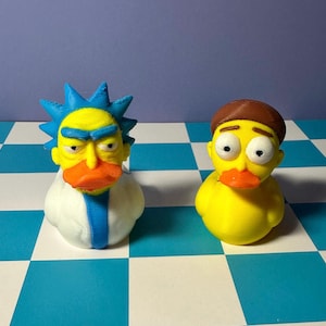 May include: Two novelty rubber ducks, one with blue spiky hair and a yellow face, the other with brown hair and a yellow face. Both ducks have orange beaks and are on a blue and white checkered surface.