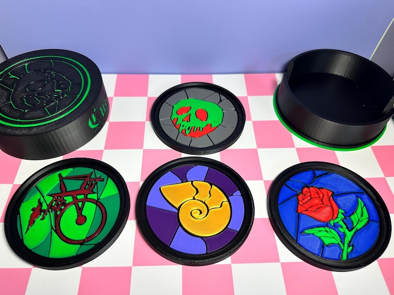 May include: A collection of round coasters with black rims and colorful designs. The designs include a green skull, a red rose, a yellow seashell, and a green and red bicycle. A black container with a green rim is also present.
